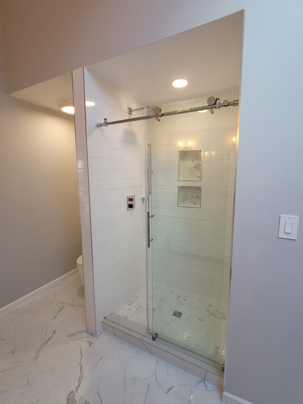 A glass-enclosed shower with a sliding door and marble-look tile flooring in a modern, neutrally colored bathroom.