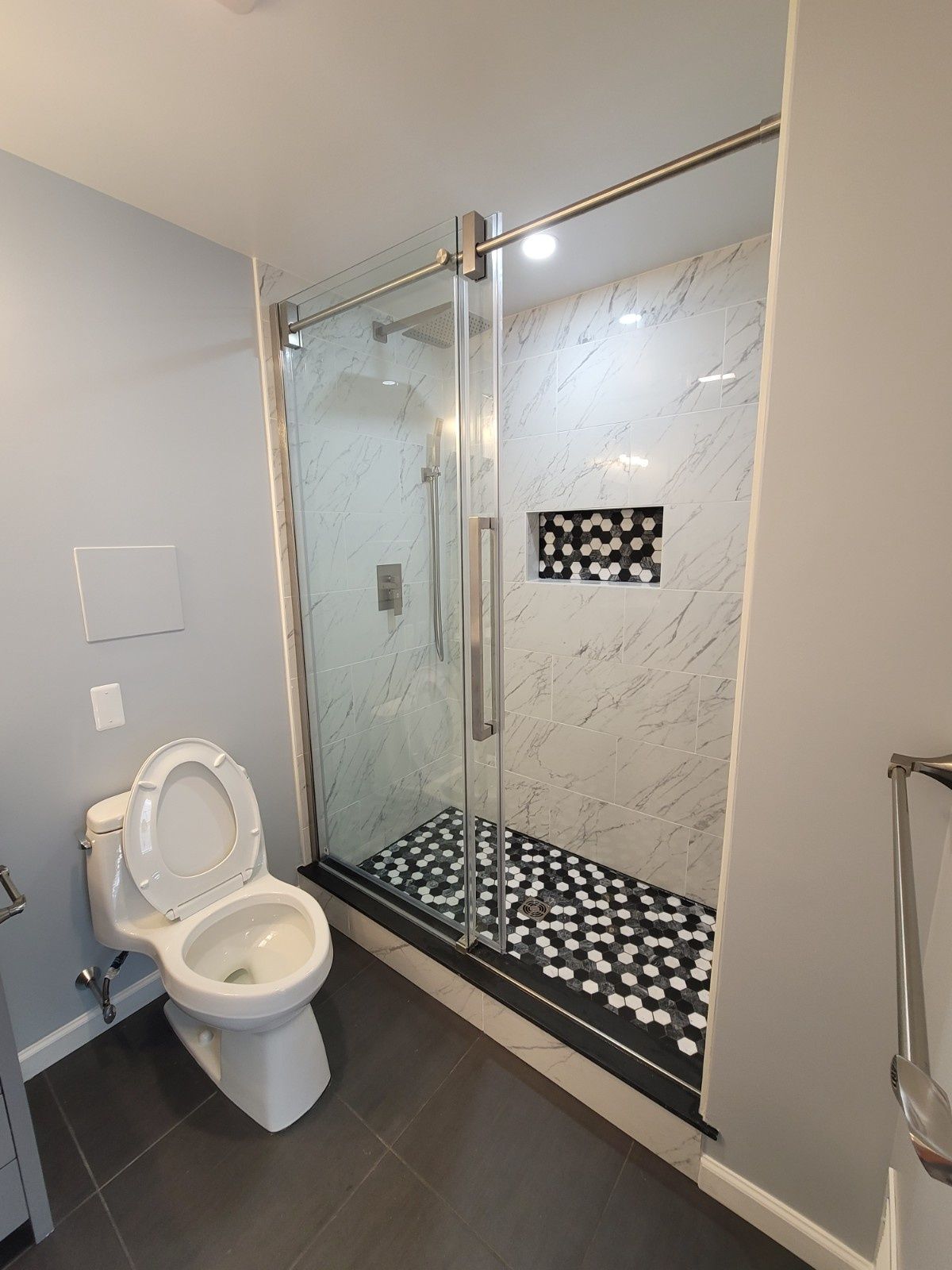 A bathroom featuring a toilet next to a glass-enclosed shower with white marble walls and a black and white tiled floor.