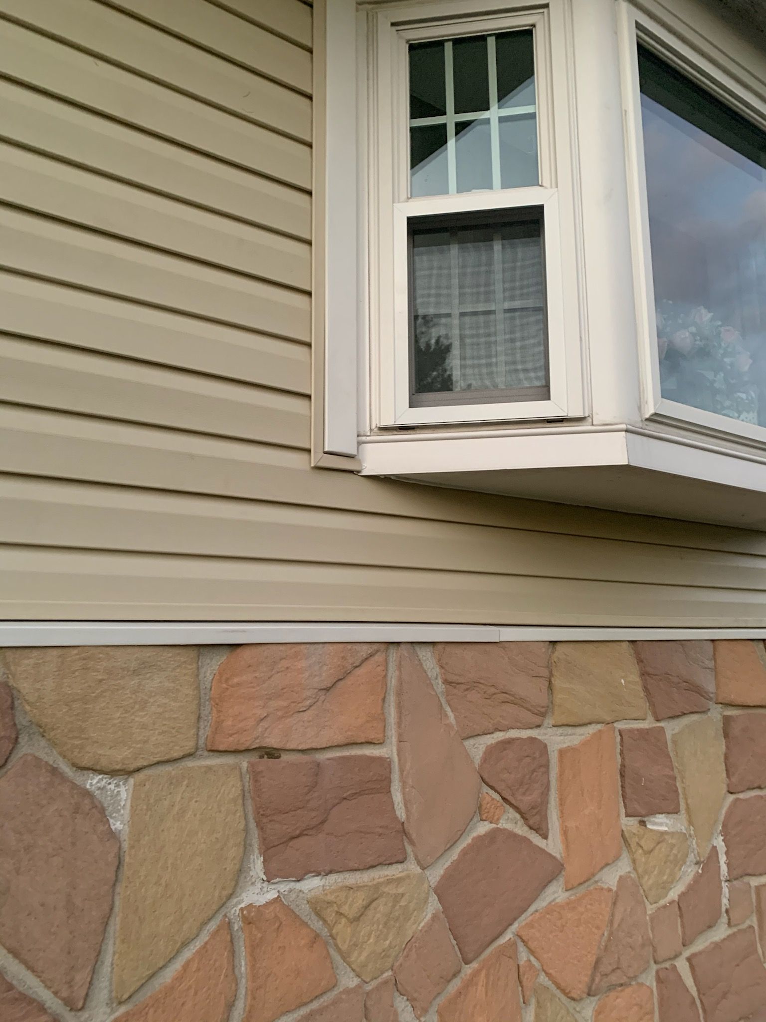 Light tan horizontal vinyl siding above a wall made of multi-colored, irregularly shaped flat stones.