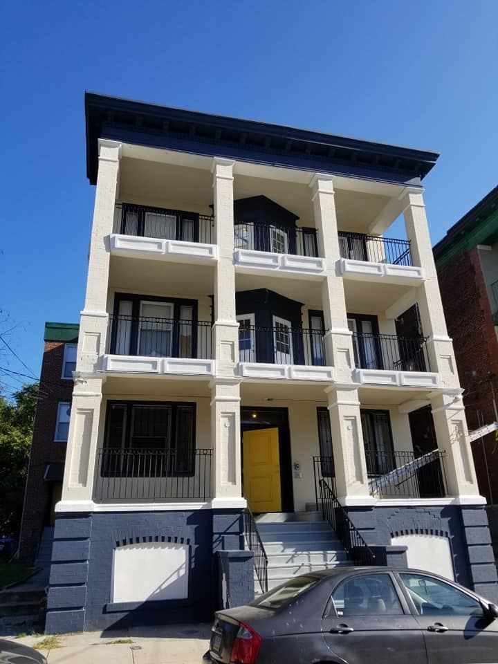 A three-story building with a navy blue exterior, cream-colored pillars, stacked porches, and a bright yellow front door.