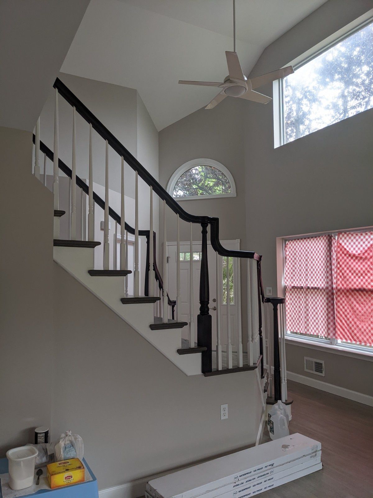 A foyer with a white staircase featuring black railings, light walls, a ceiling fan, and windows with red patterned blinds.