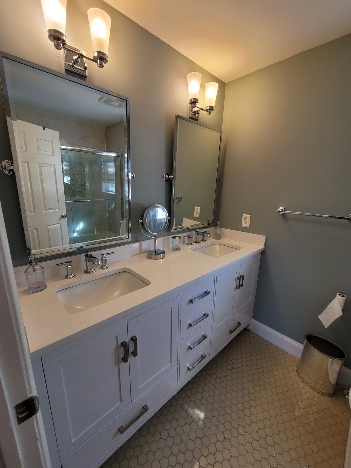Modern bathroom with a double white vanity, gray walls, two framed mirrors, and honeycomb-patterned tile floor.