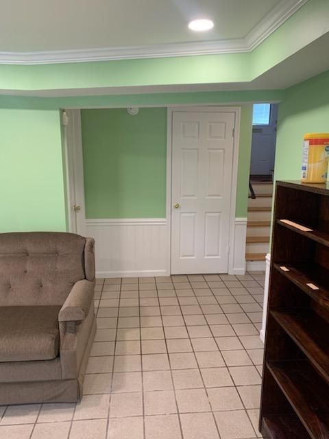 A room with light green walls, beige tile floors, a brown sofa, a dark wooden bookshelf, and a white door near stairs.