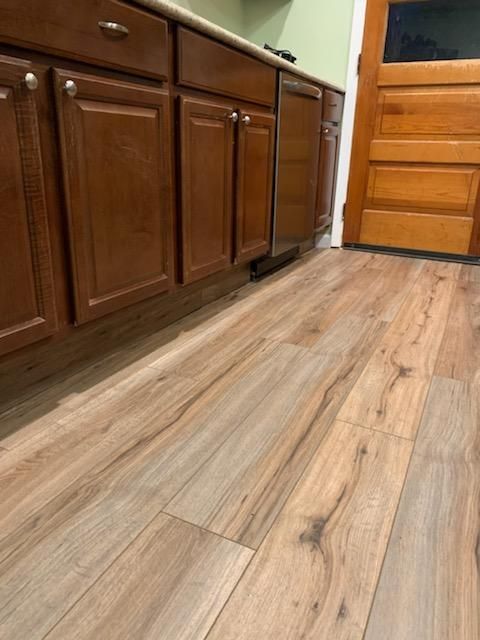 A low-angle view of wood-look flooring next to cherry-colored wooden cabinets and a matching door in a kitchen.