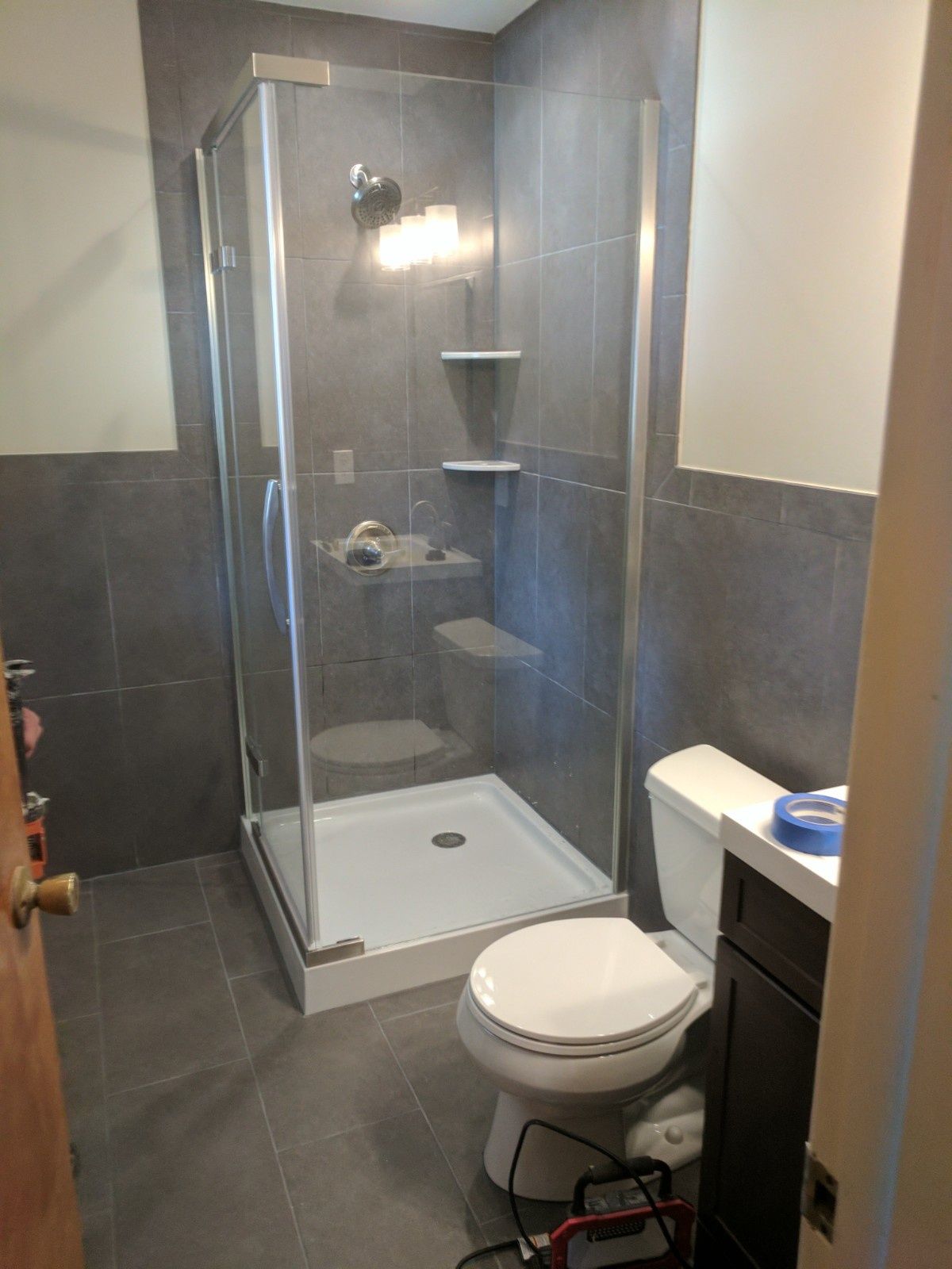 A modern bathroom featuring a walk-in glass shower with gray tile walls, a white toilet, and a dark wood vanity.