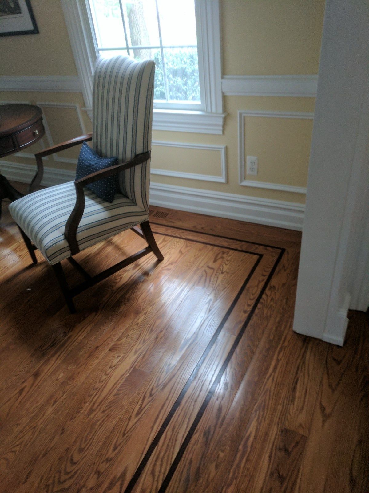A striped upholstered armchair sits on hardwood flooring featuring a dark wood border inlay in a room with light walls.