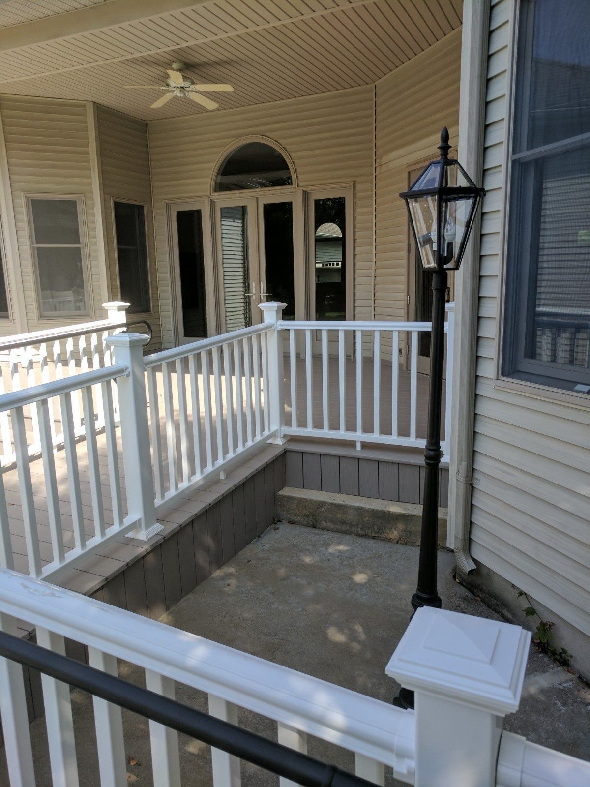 A white-railed deck with a concrete landing, a dark lamp post, and an arched doorway leading to a house exterior.