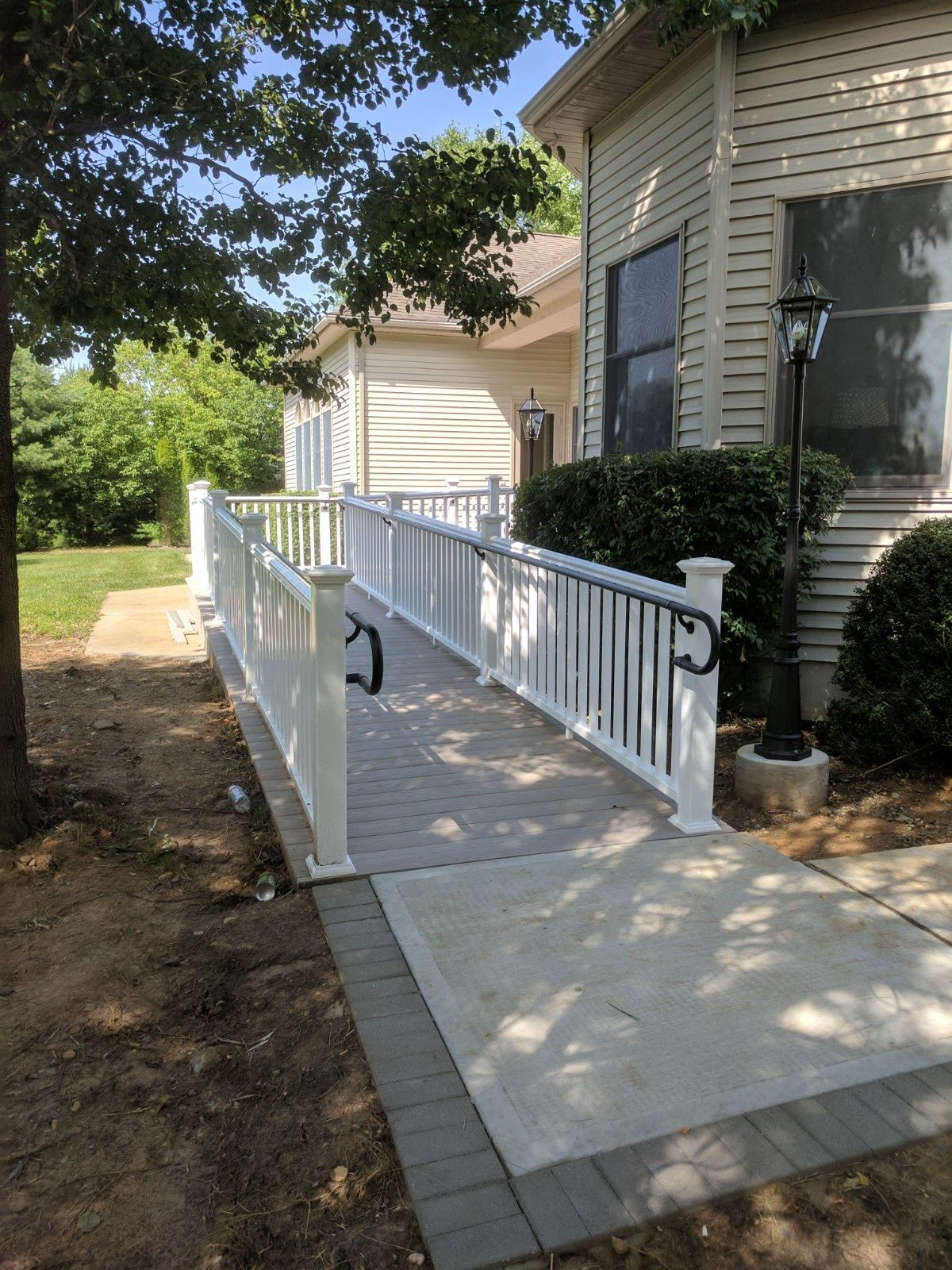 A white vinyl ramp with handrails leading to the entrance of a beige residential home on a sunny day.