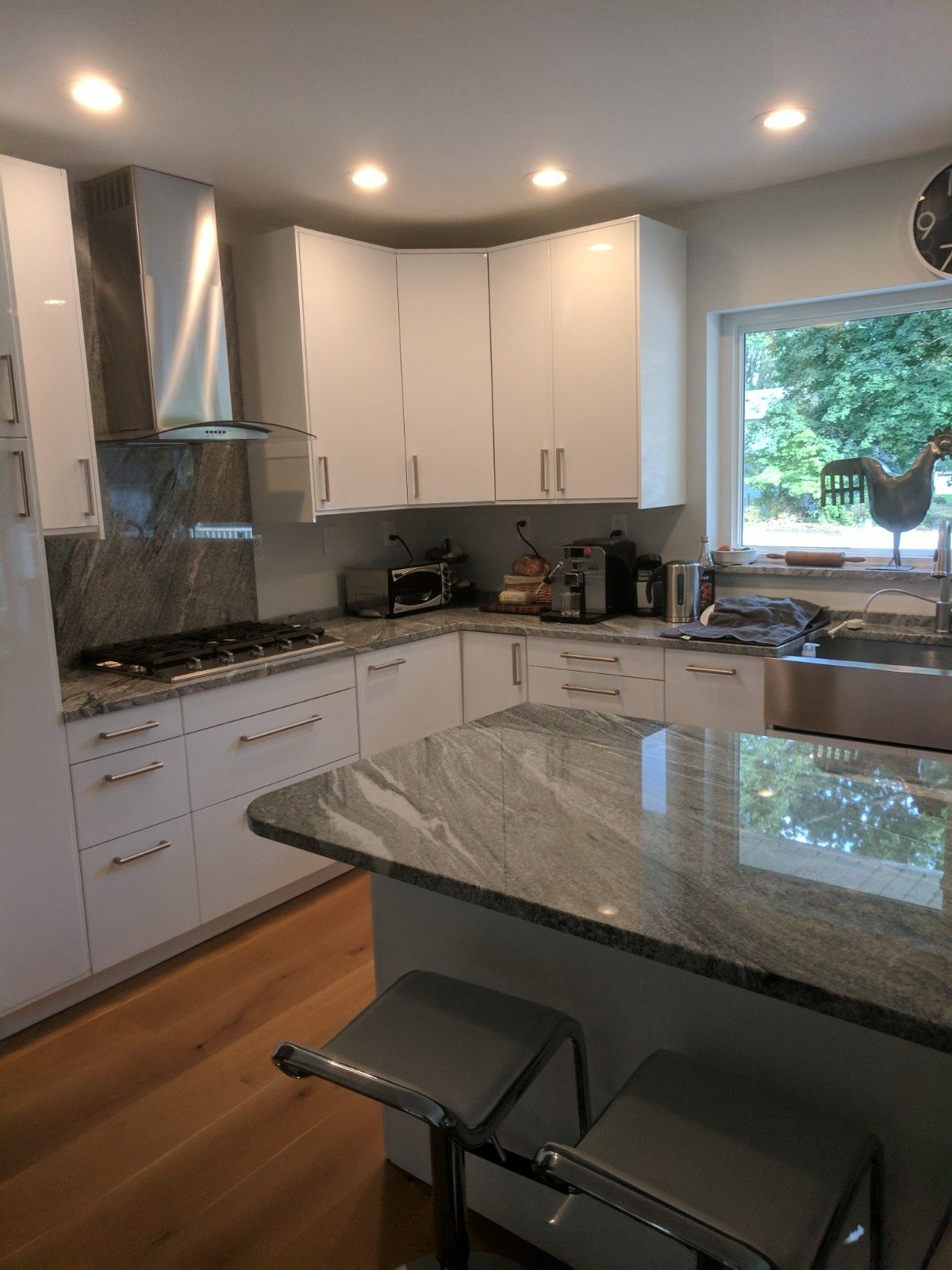 A modern kitchen featuring white cabinets, grey granite countertops, a stainless steel hood, and a central island with stools.