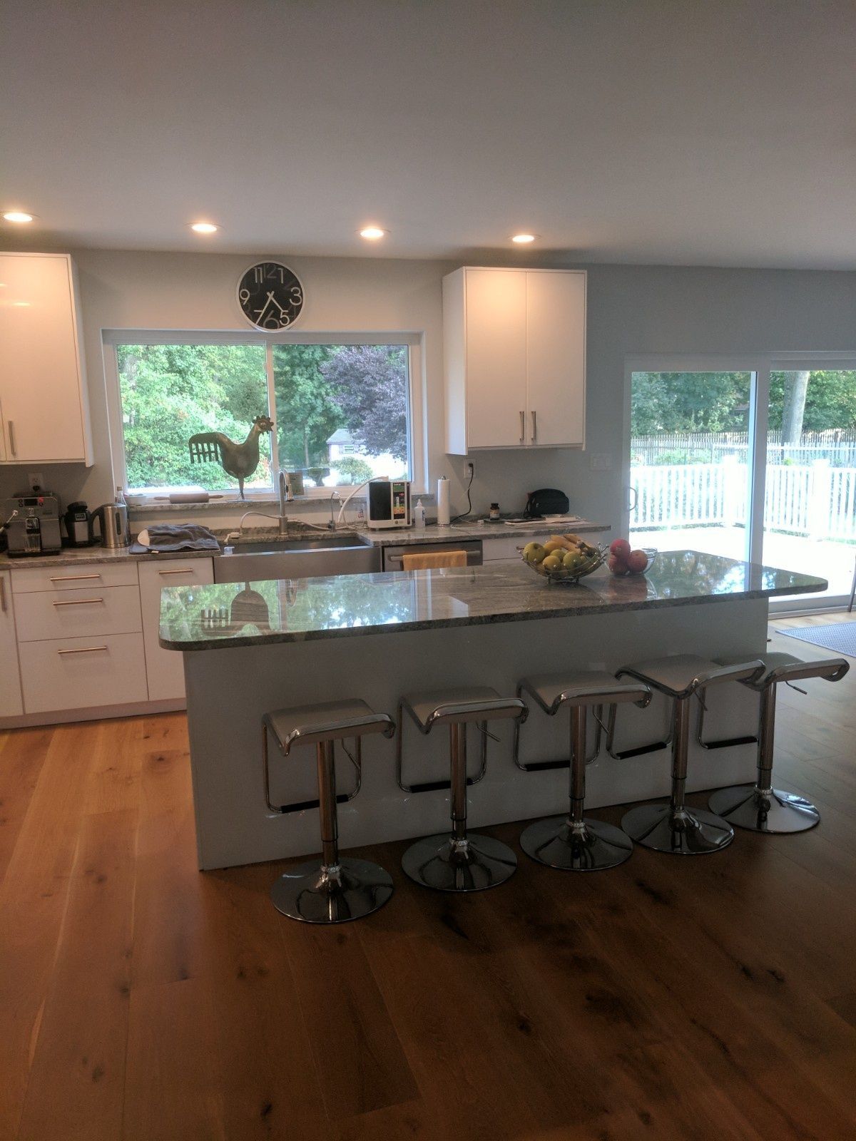Modern kitchen featuring white cabinets, a granite island with four barstools, and light hardwood floors.