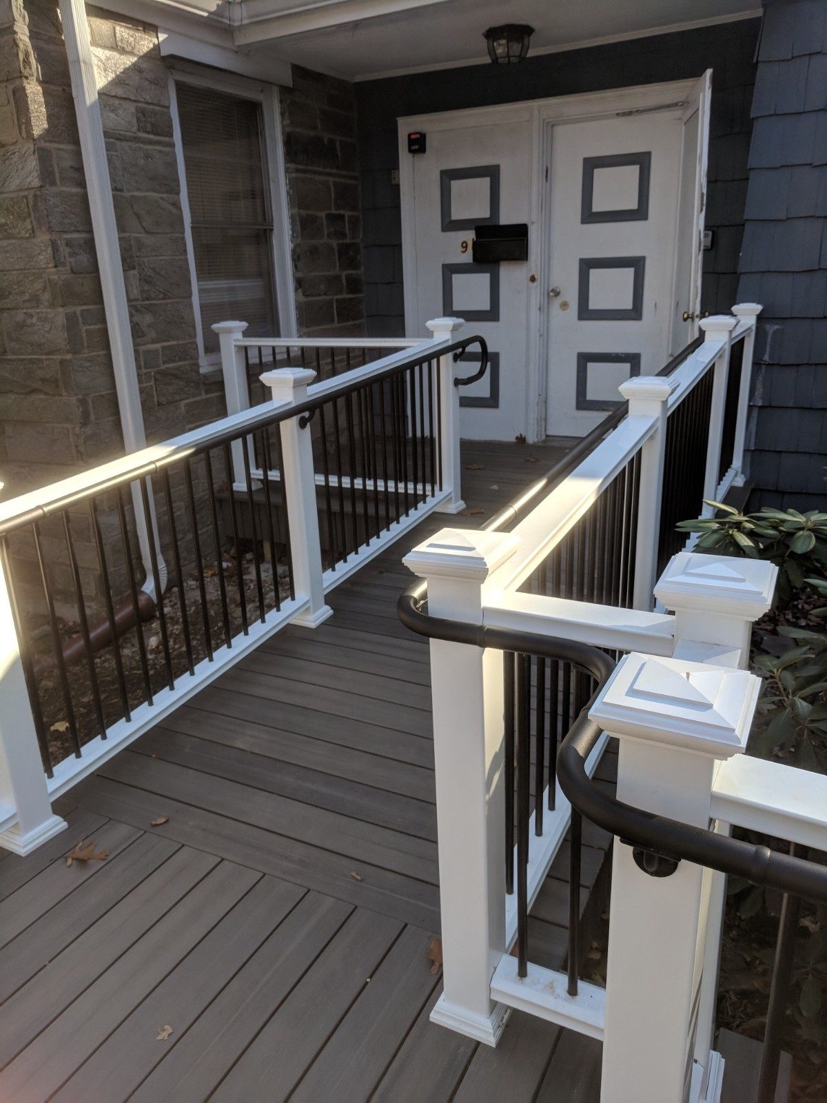 A wooden wheelchair ramp with white railings and black metal spindles leading to double doors on a stone building.