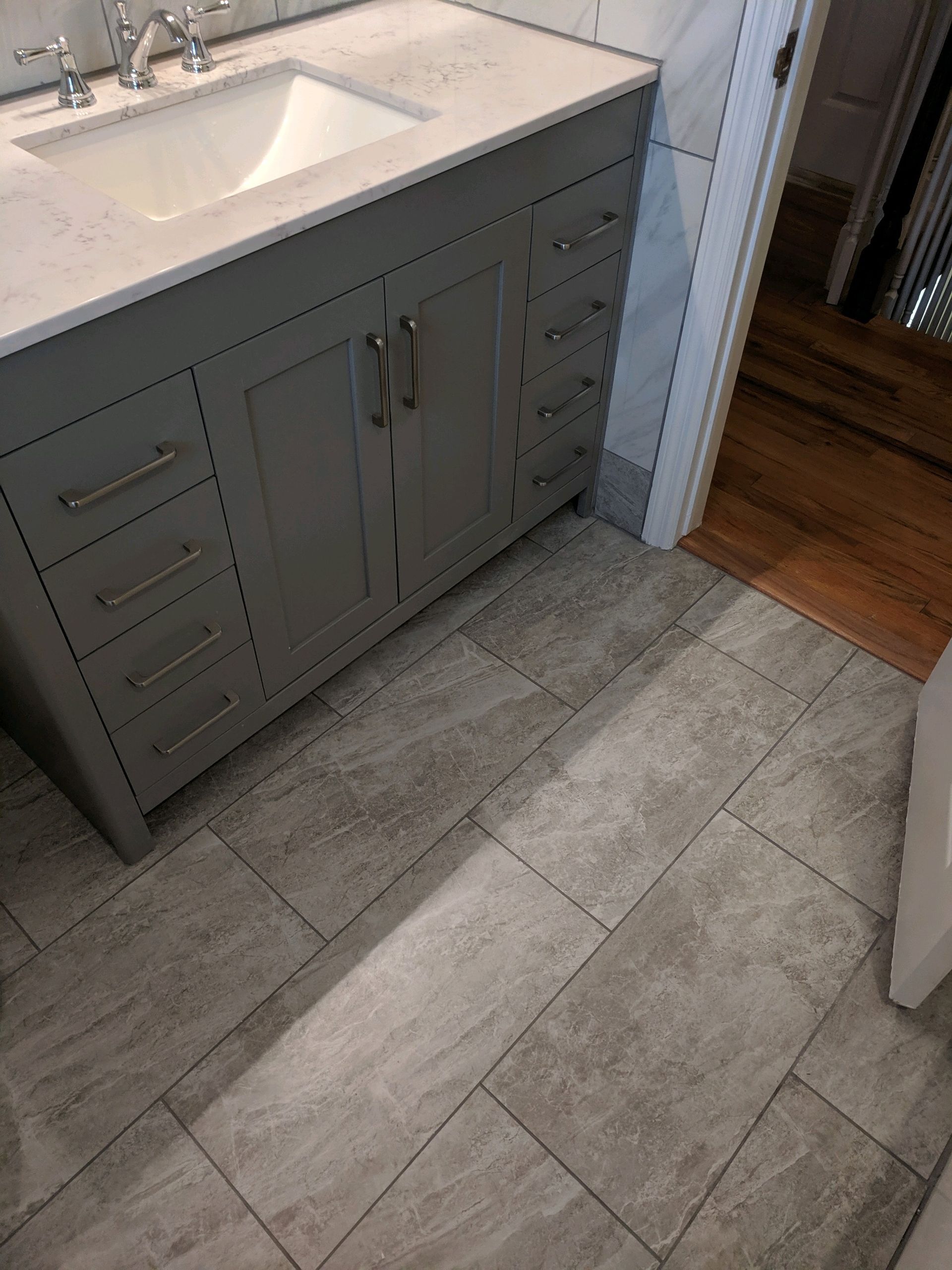A gray bathroom vanity with a white countertop and sink, set on a gray tiled floor next to a doorway.