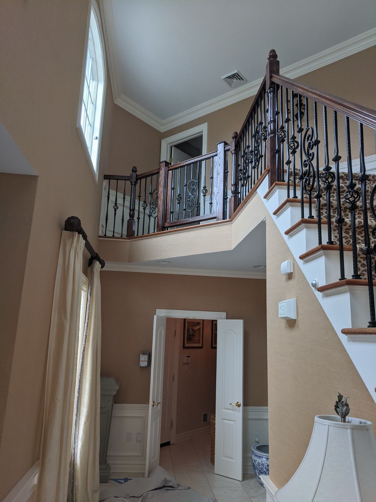 An entryway with tan walls, white wainscoting, a staircase with black iron railings, and a doorway leading to a room.