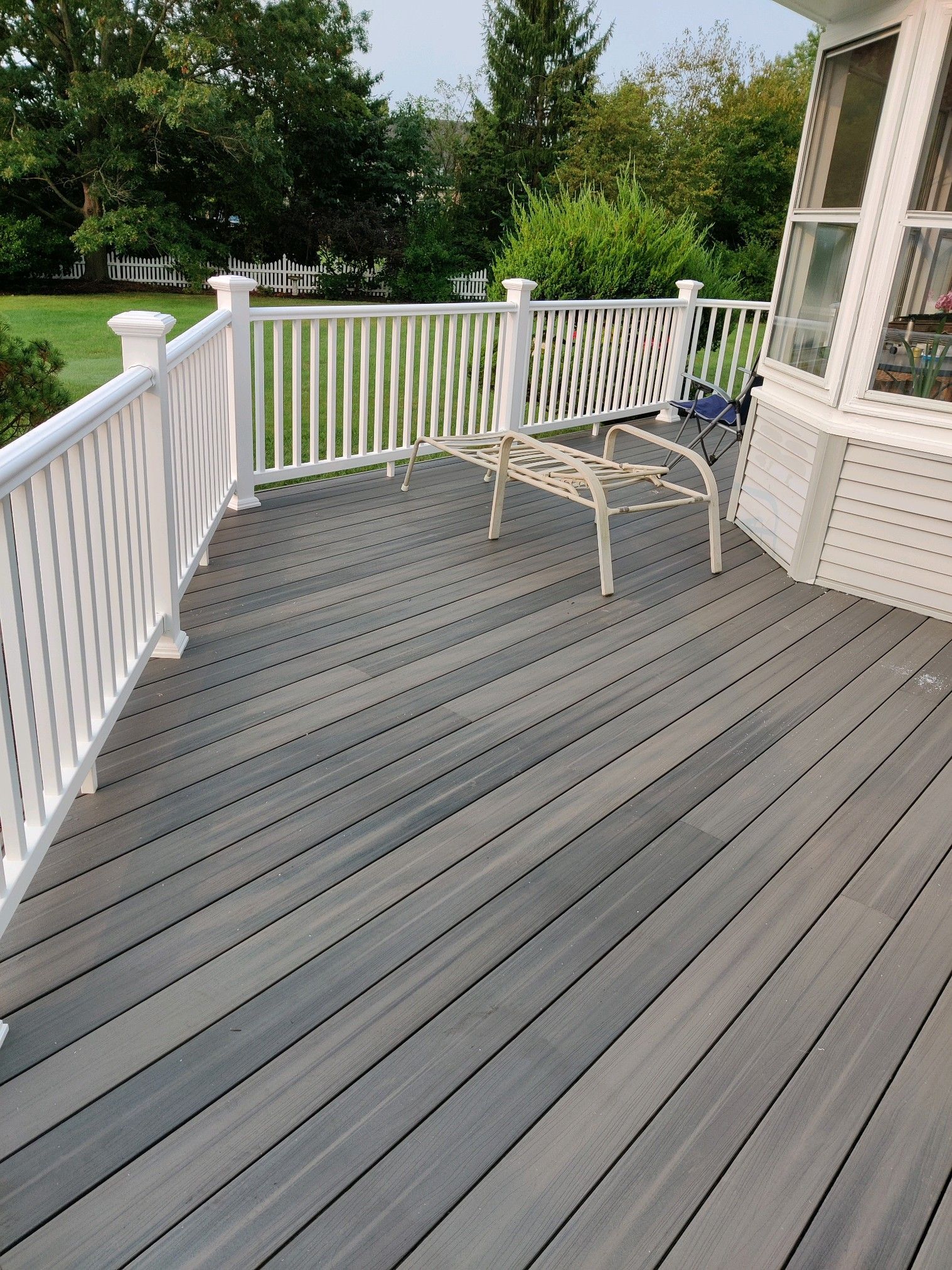 A gray composite deck with white railings and lattice accents, featuring a small metal bench against a house corner.