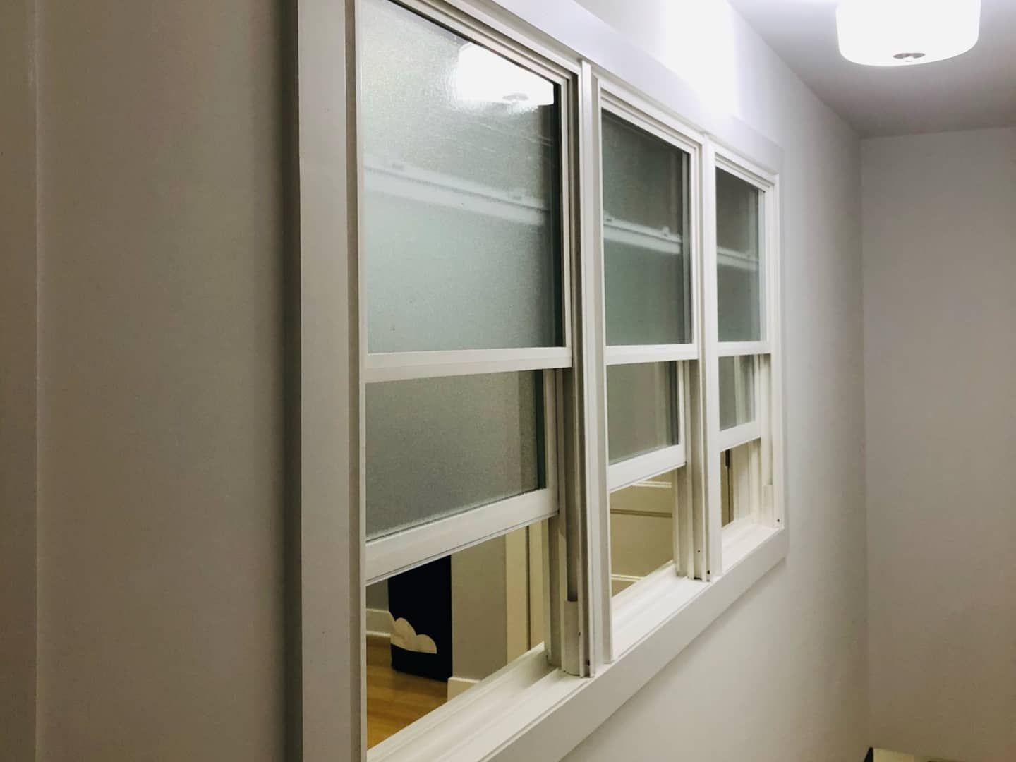 A side view of a white, multi-pane window with frosted glass in a room with light-colored walls.