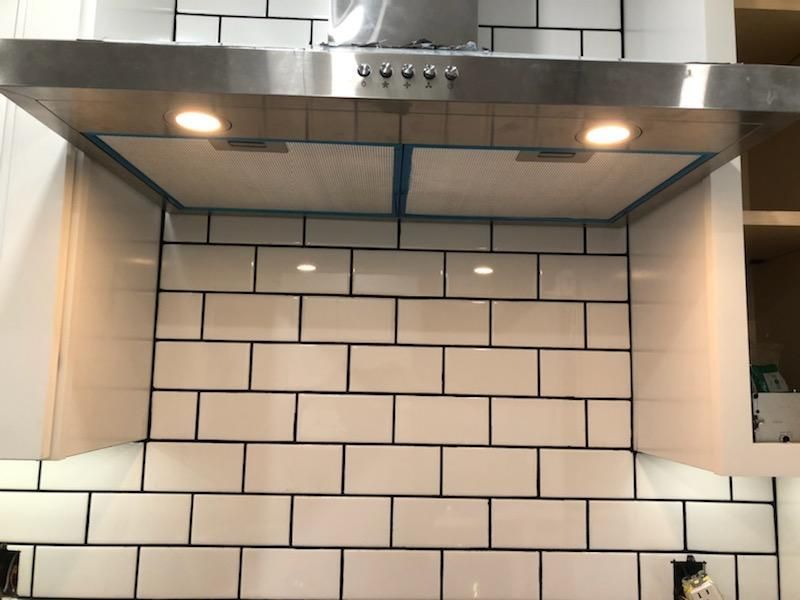 A stainless steel range hood with two glowing lights mounted above a white subway tile backsplash in a kitchen.