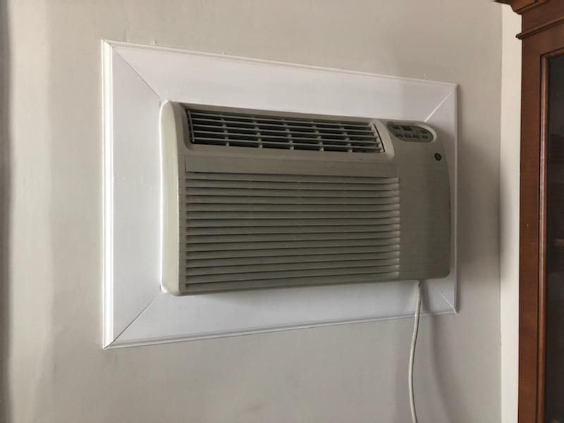 A beige wall-mounted air conditioner unit installed in an interior wall with a white rectangular trim frame.