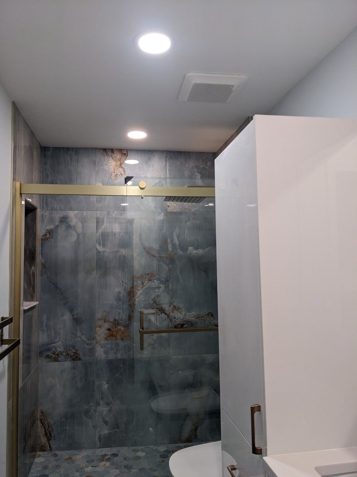 A modern bathroom shower with dark, marble-patterned tile, gold hardware, and recessed ceiling lighting.