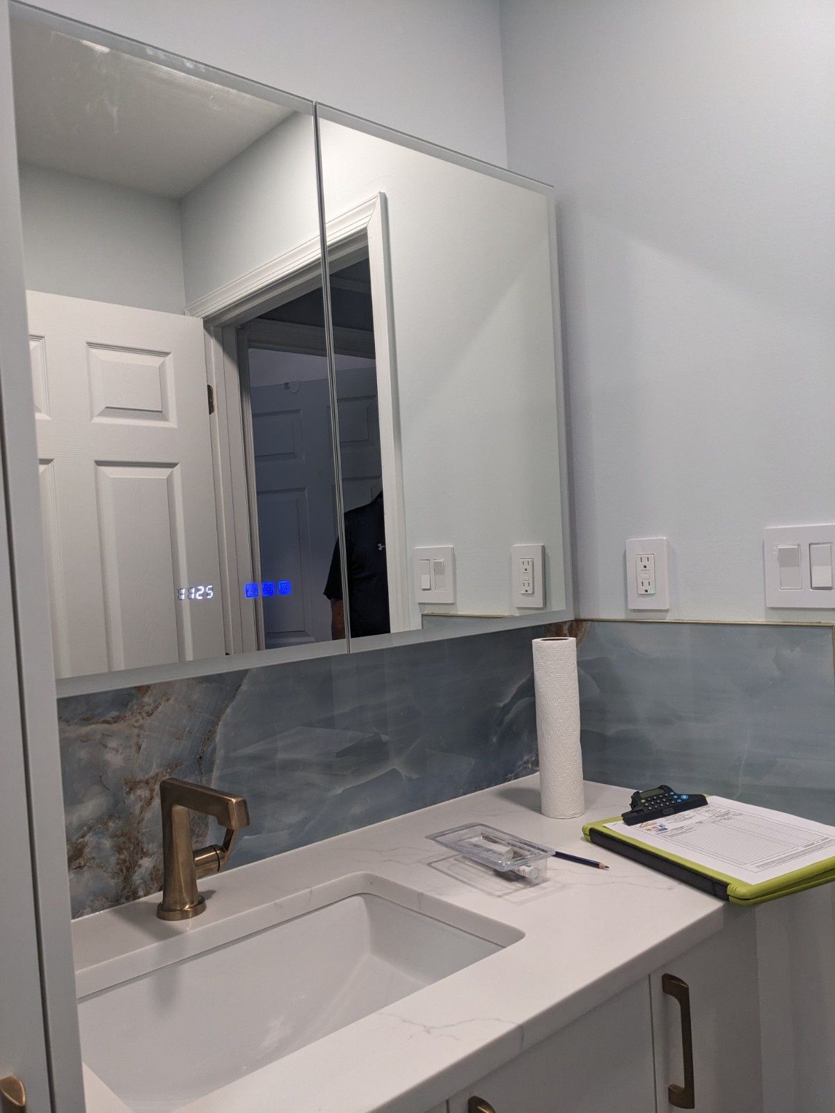 A modern bathroom vanity with a white countertop, gold faucet, blue tiled backsplash, and a large mirrored cabinet.