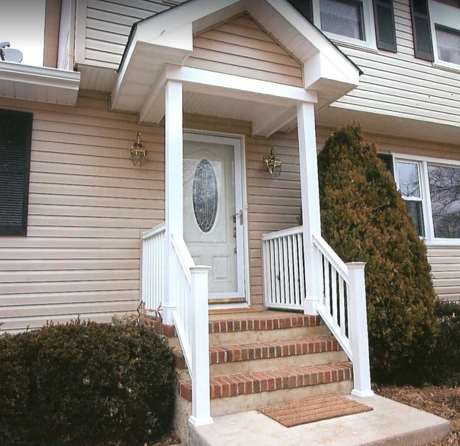 A front entrance with tan vinyl siding, a white portico, white railings, and brick steps leading to a white front door.