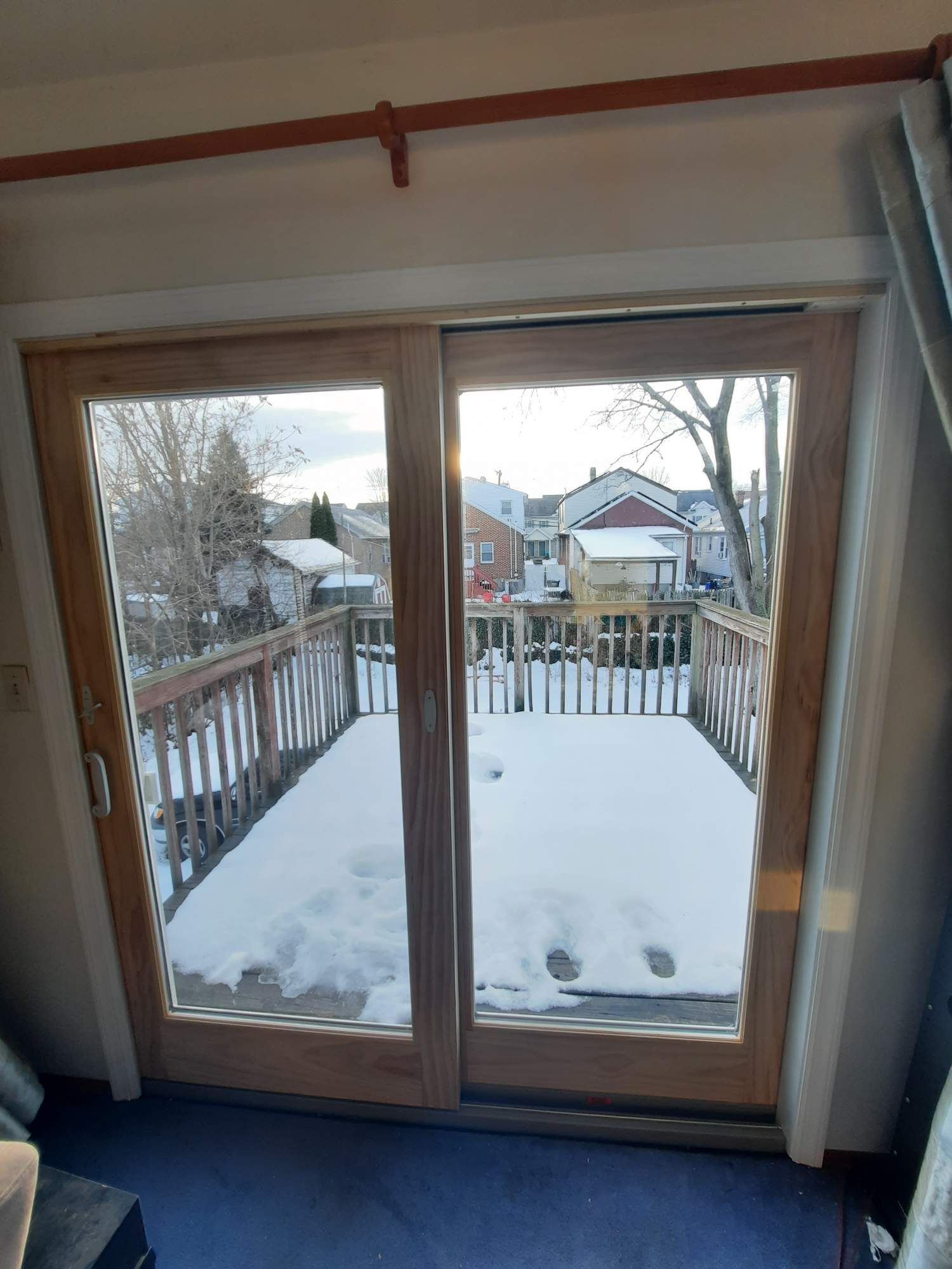 A sliding glass door looking out onto a snow-covered wooden deck with houses in the background.