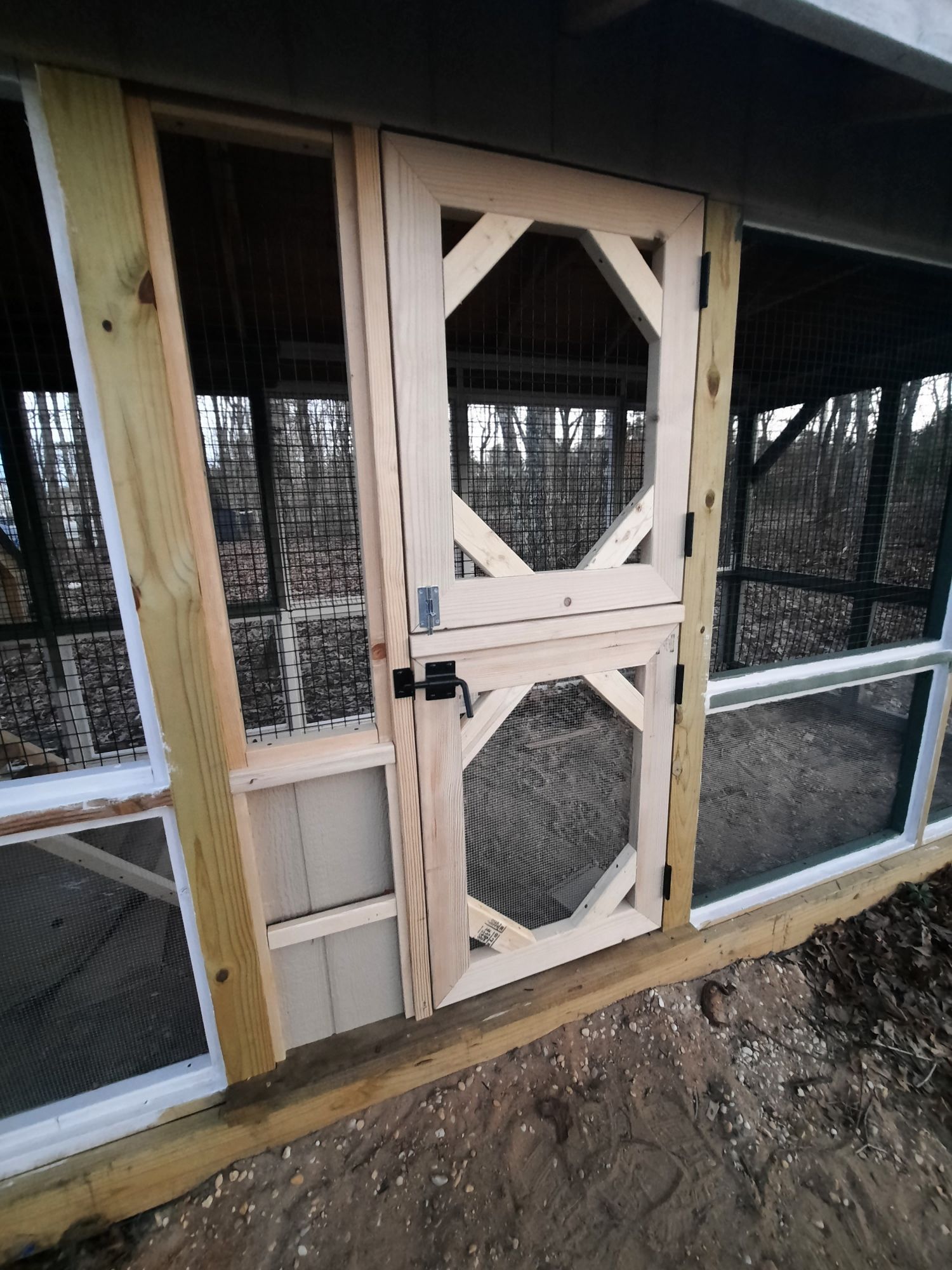 A light-wood Dutch-style door with wire mesh panels set in a wooden frame structure, likely a chicken coop or outdoor pen.