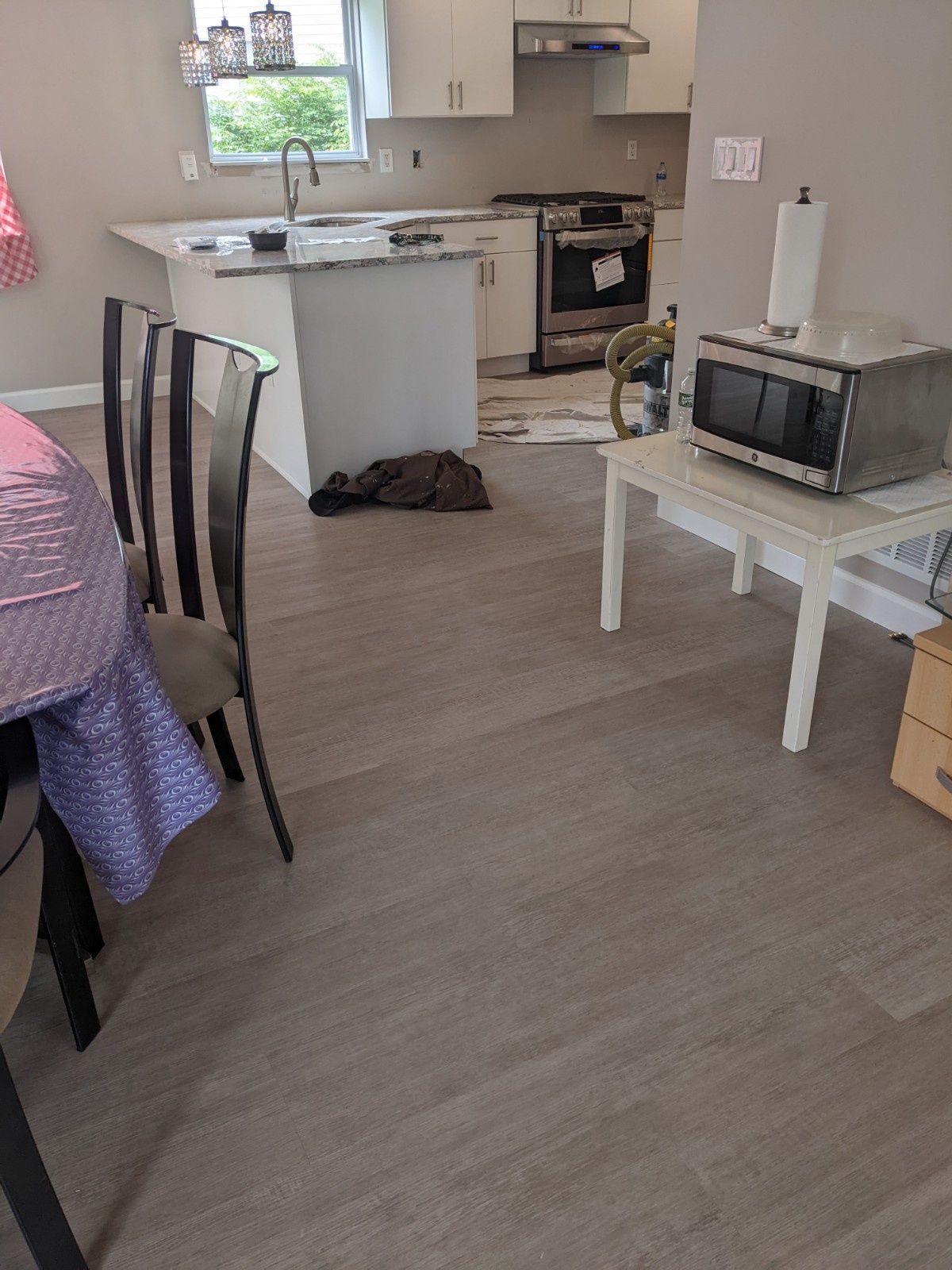 A dining area with a purple-covered table, chairs, and a white side table holding a microwave, with a kitchen beyond.
