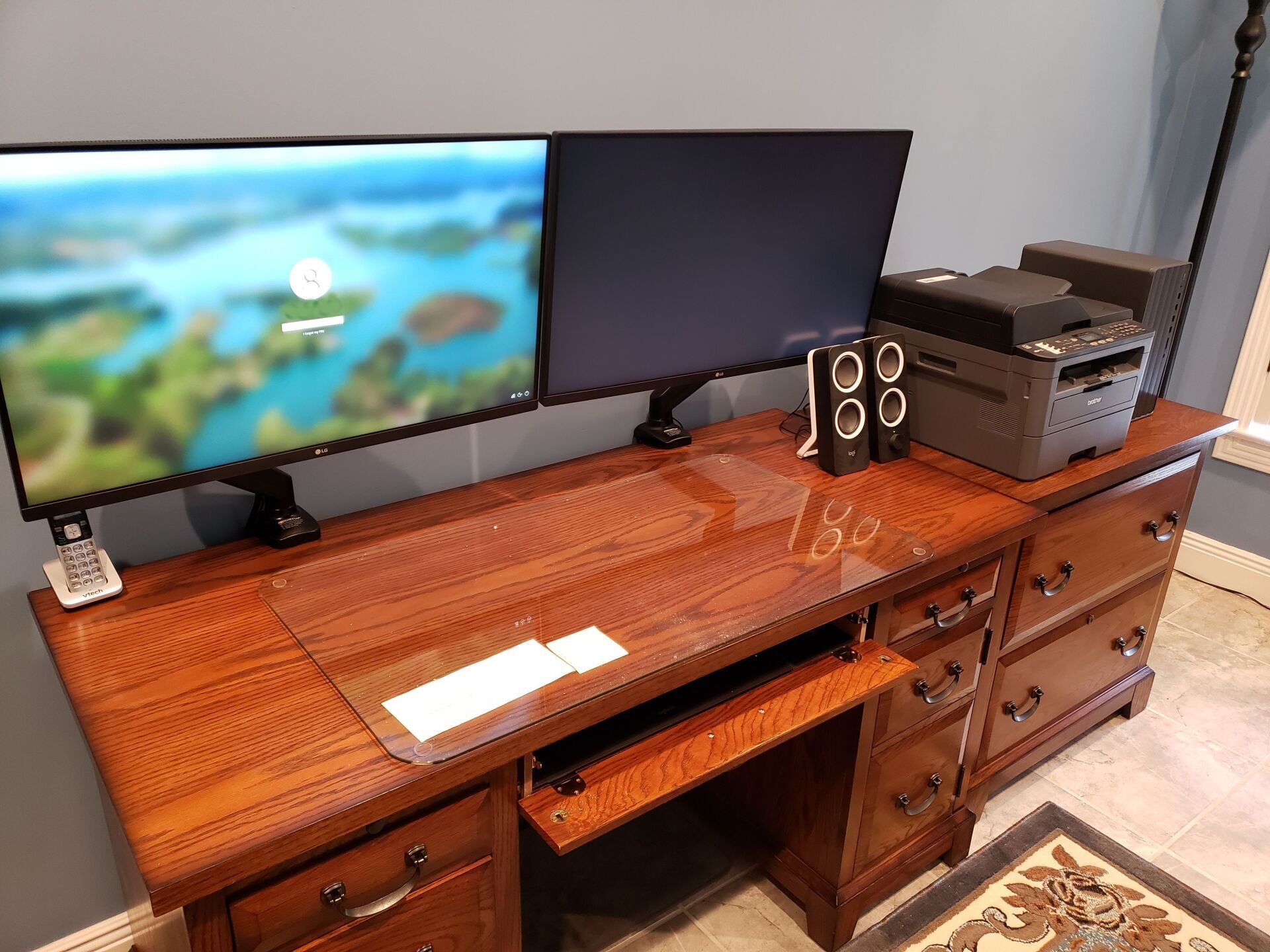 A wooden desk with two monitors and a printer on it.