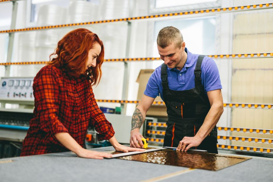 A man and a woman are working on a piece of glass in a factory.
