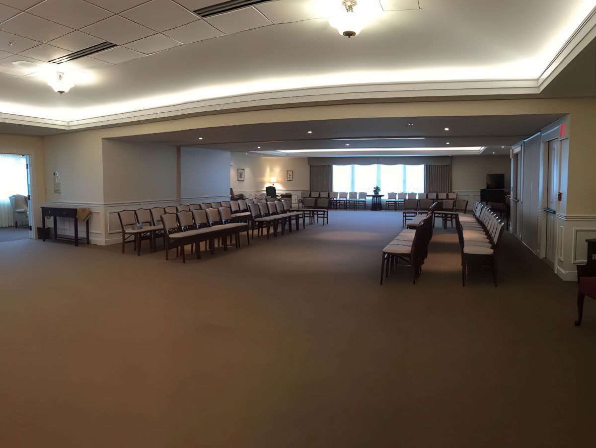 Empty beige room with rows of chairs, likely a funeral home.