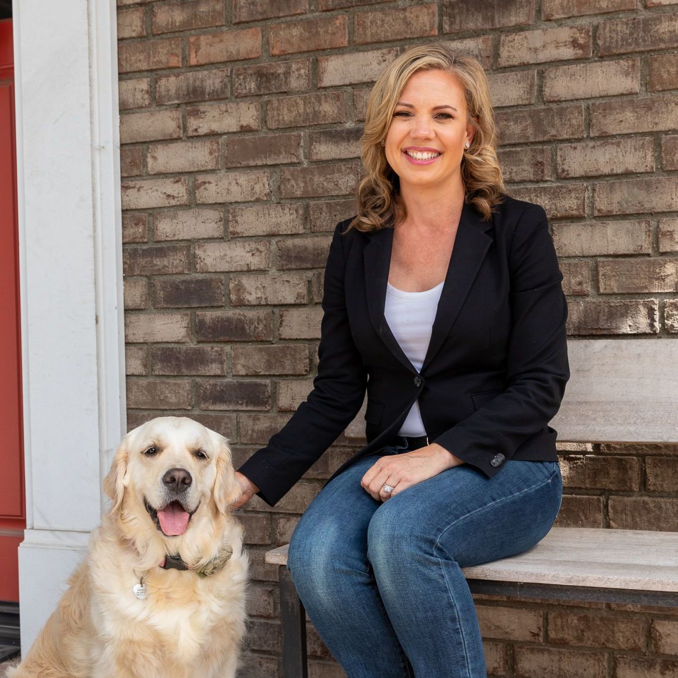 A woman is sitting on a bench next to a dog