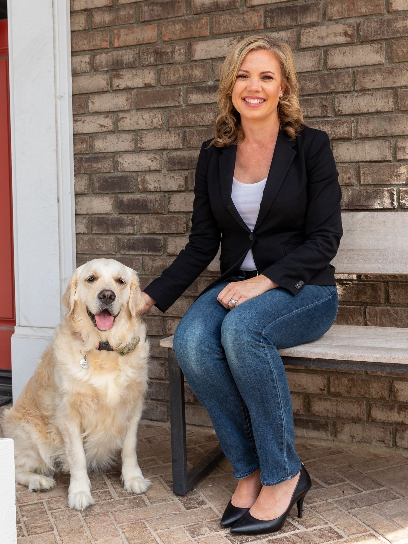 A woman is sitting on a bench next to a dog.