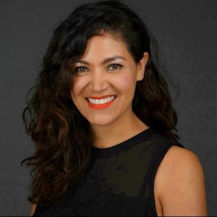 A woman wearing a black dress and red lipstick is smiling for the camera.