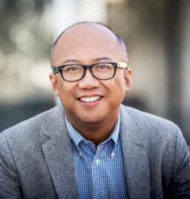 A man wearing glasses and a suit is smiling for the camera