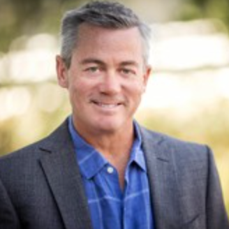 A man in a suit and blue shirt is smiling for the camera.