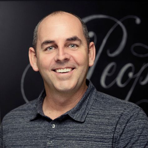 A man in a blue shirt is smiling in front of a sign that says people.