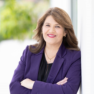 A woman in a purple jacket is leaning against a wall and smiling.