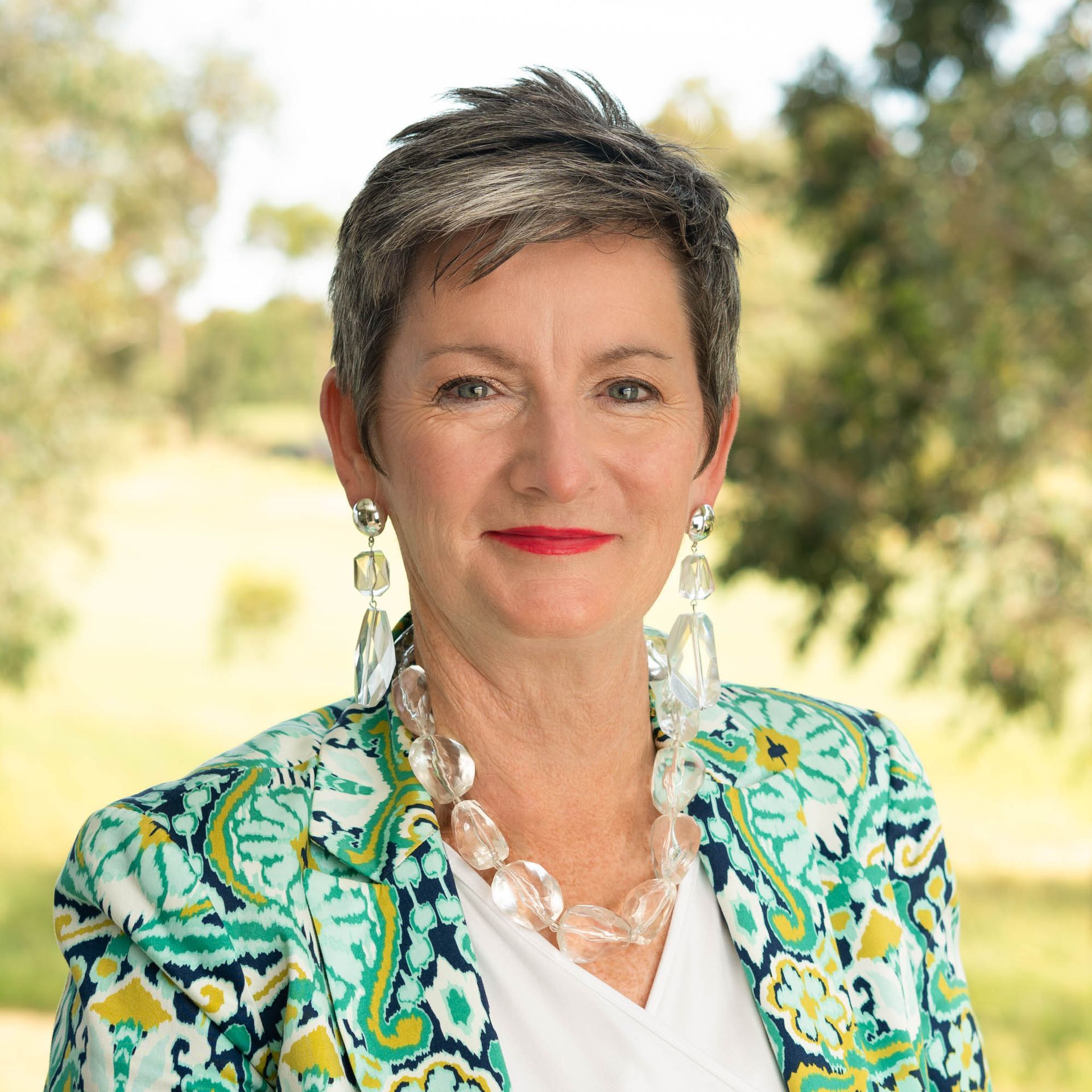A woman wearing a green jacket and earrings is smiling for the camera.