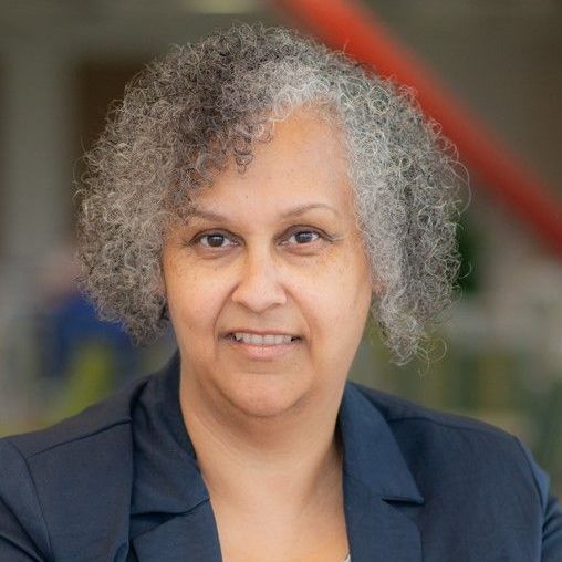 A woman with curly hair is wearing a blue jacket and smiling for the camera.