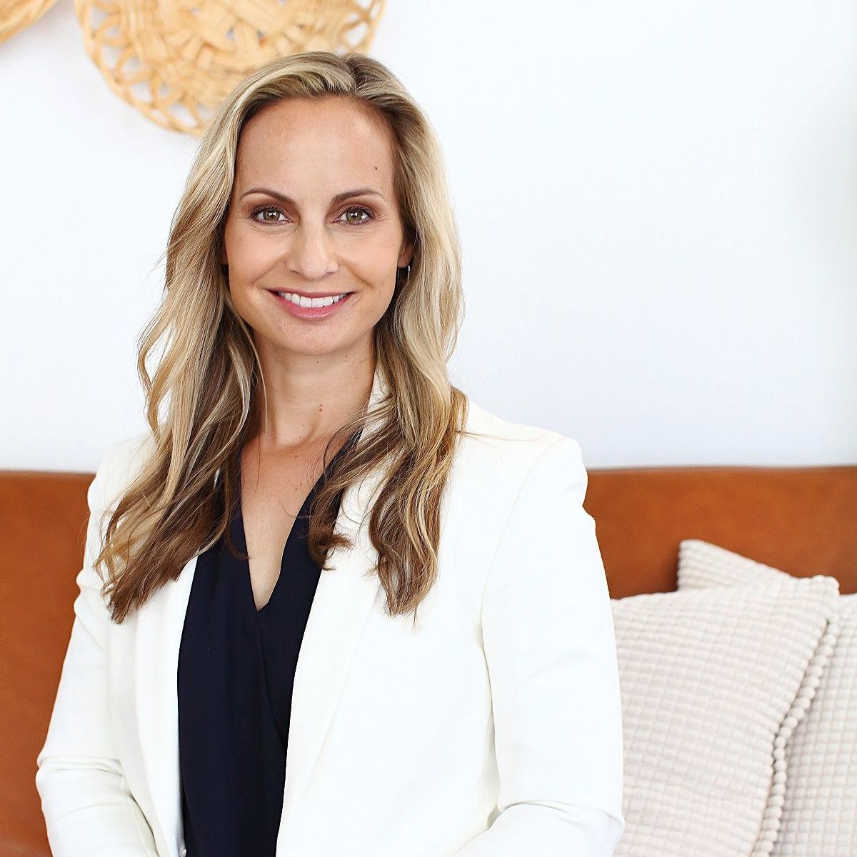 A woman is sitting on a couch wearing a white jacket and smiling.