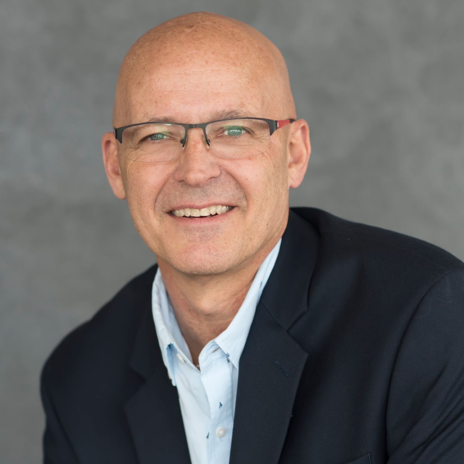 A bald man wearing glasses and a suit smiles for the camera