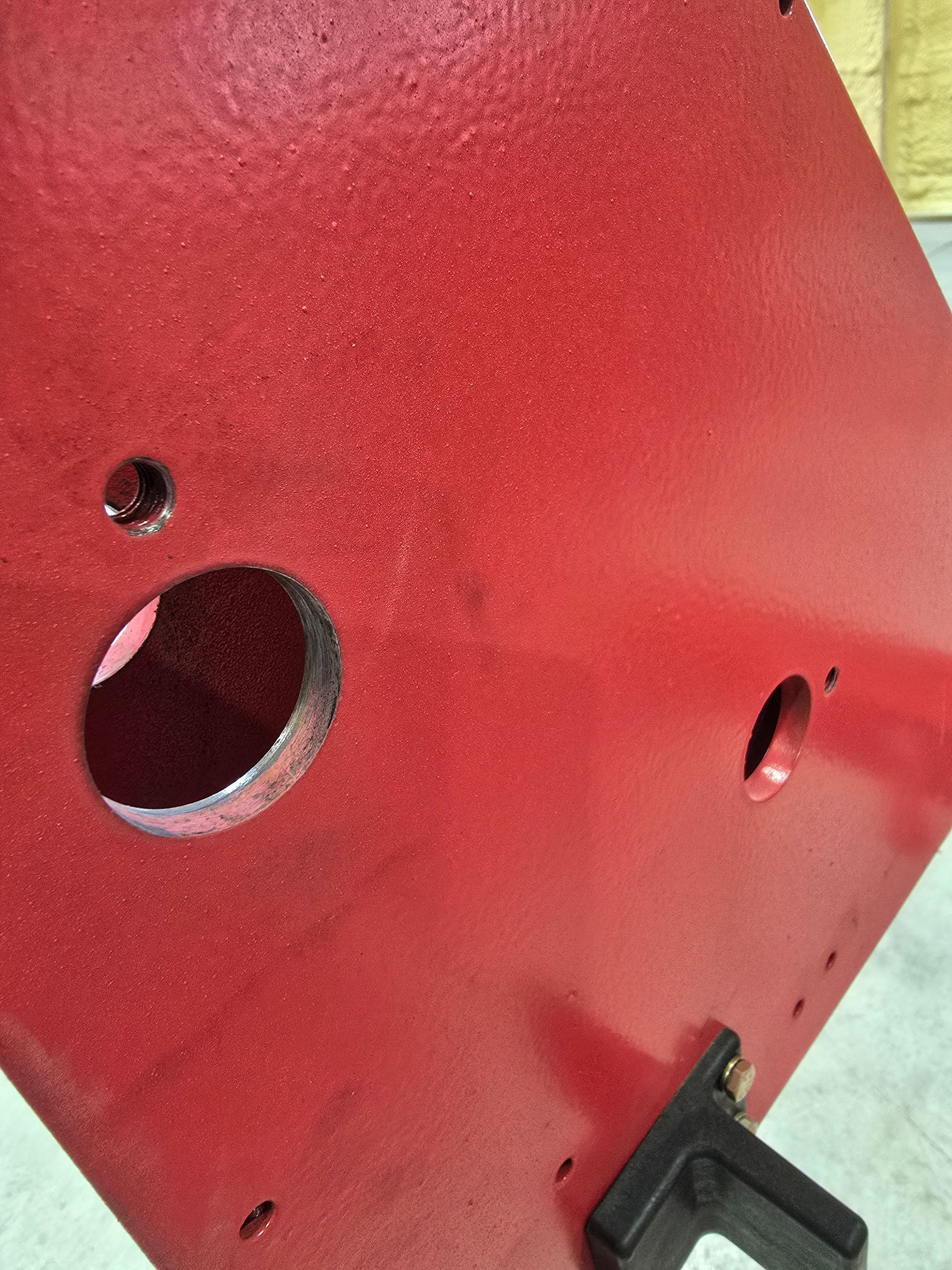 Red painted metal panel with several holes and a black bracket at the bottom edge