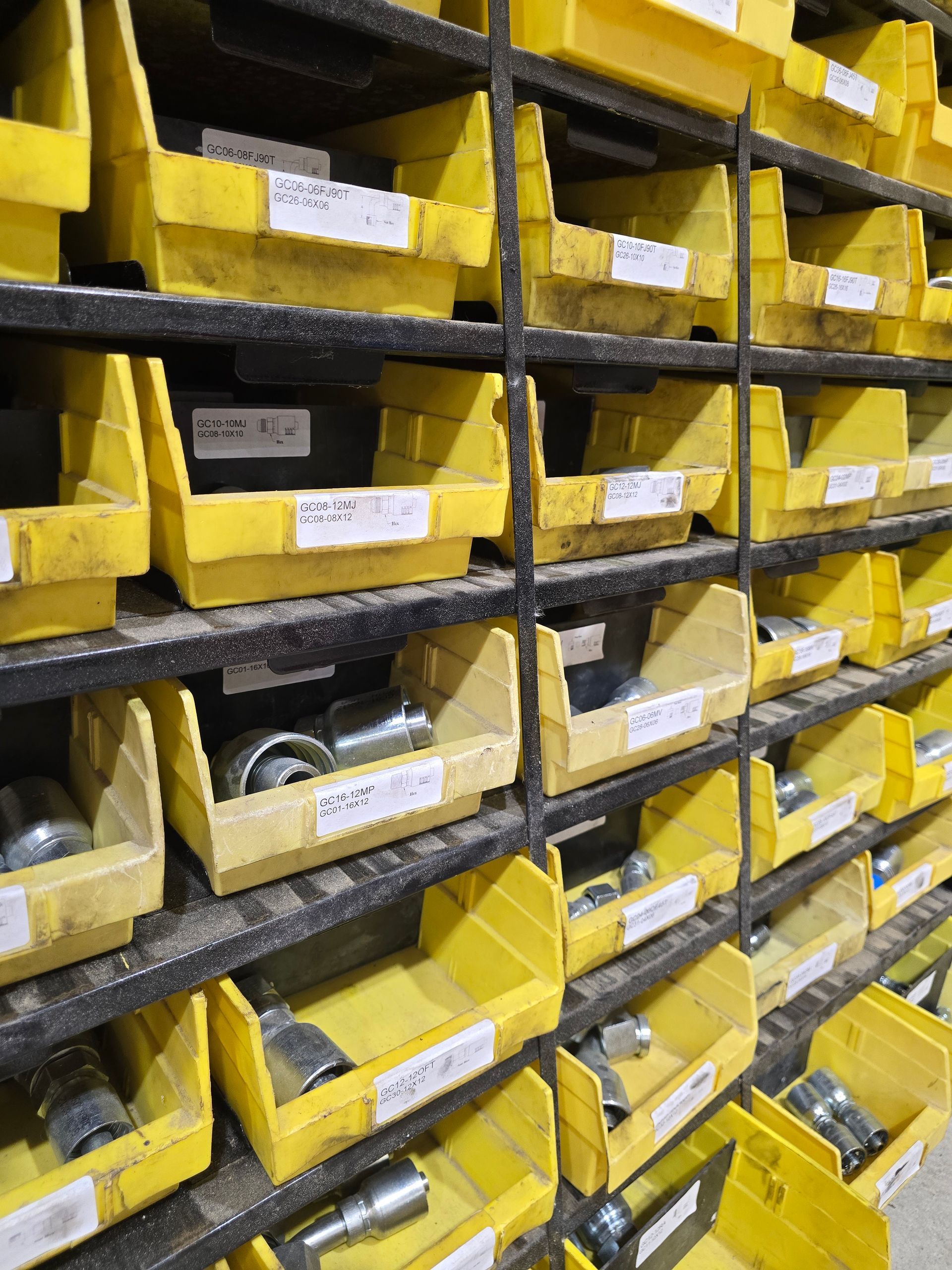 Yellow plastic parts bins stacked on metal shelves in a warehouse storage area