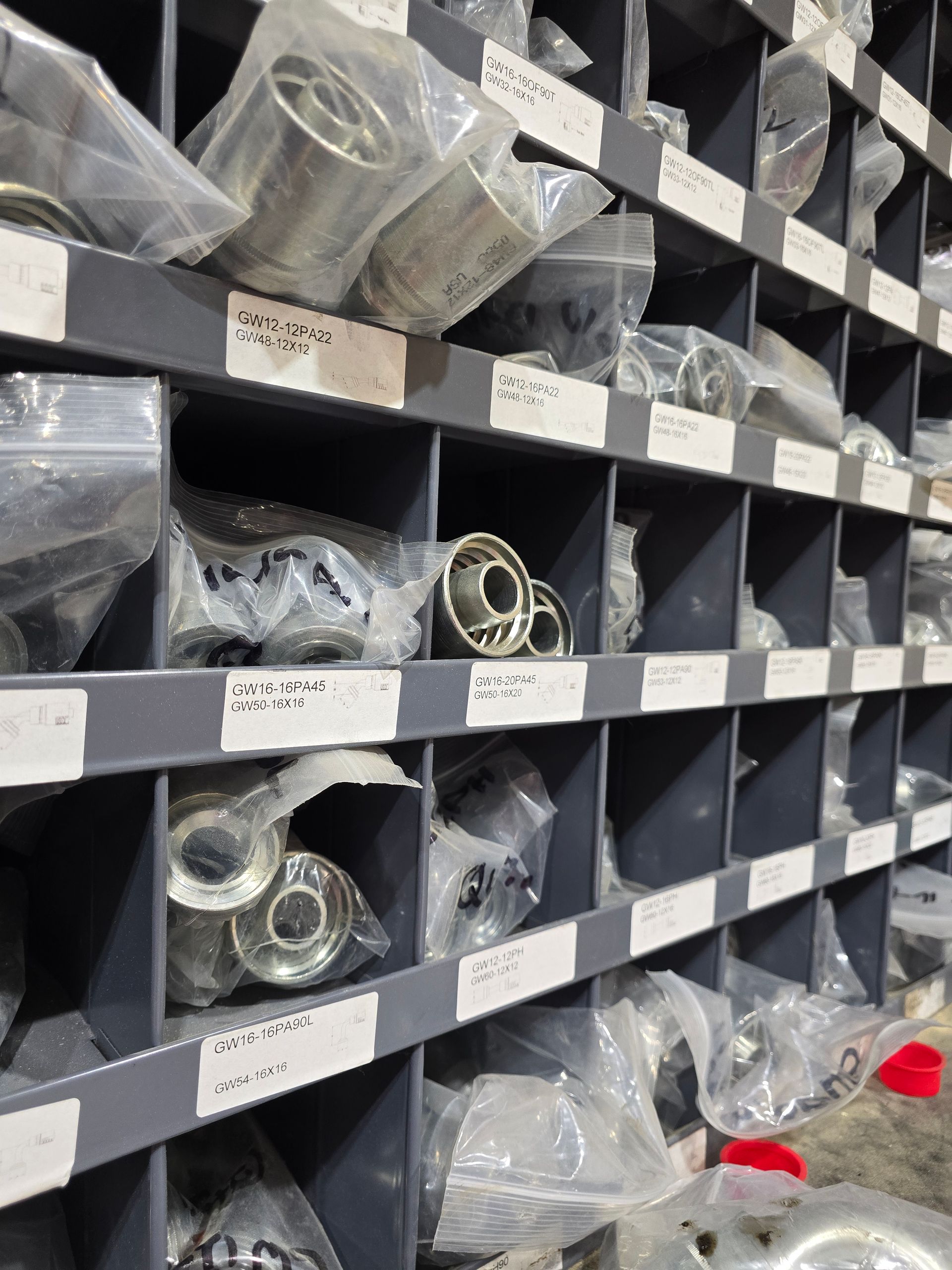 Shelves of labeled plastic bags holding metal hardware parts in a storage area