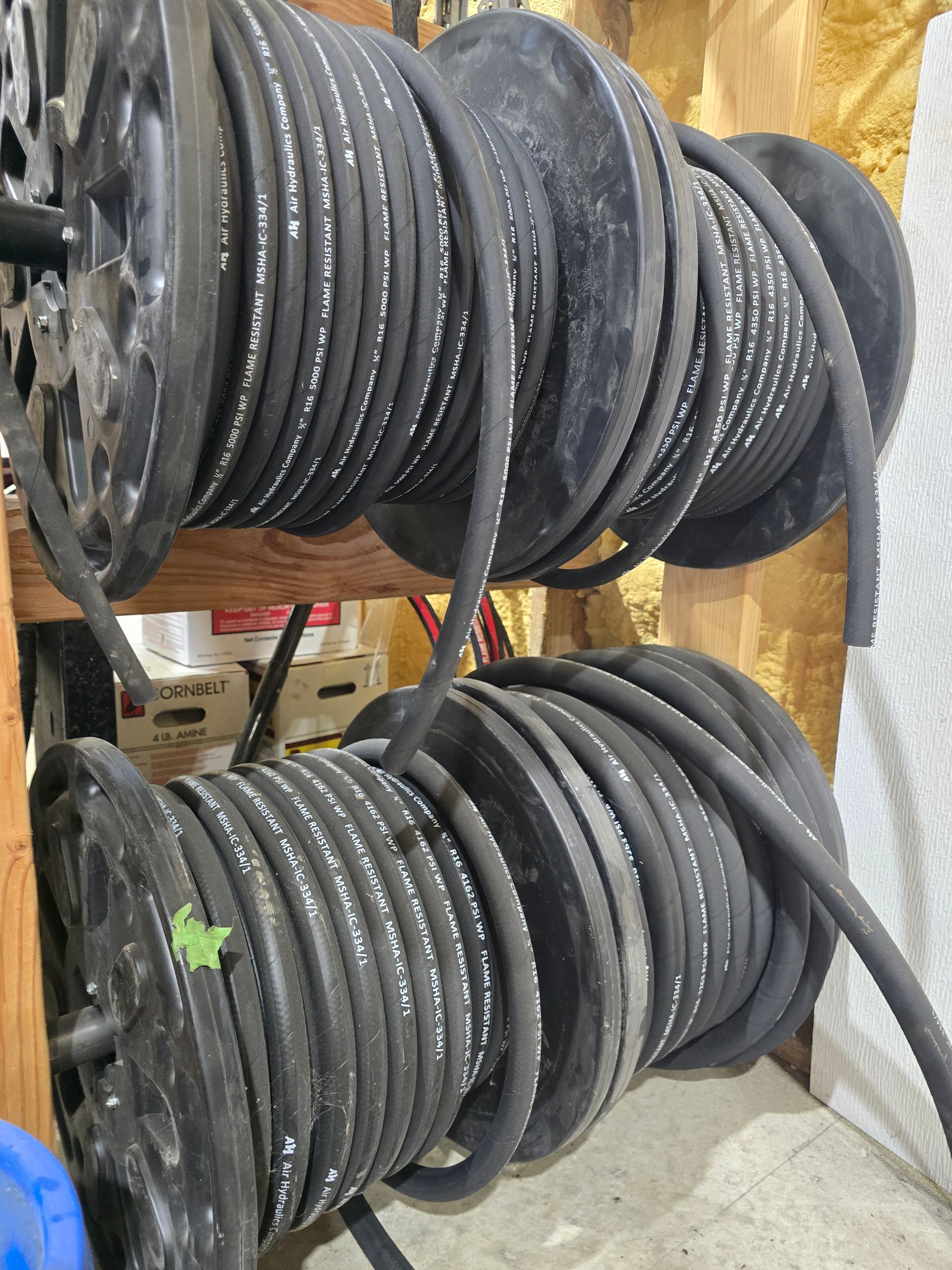Stacks of coiled black cables or hoses on wooden shelves in a workshop or storage area
