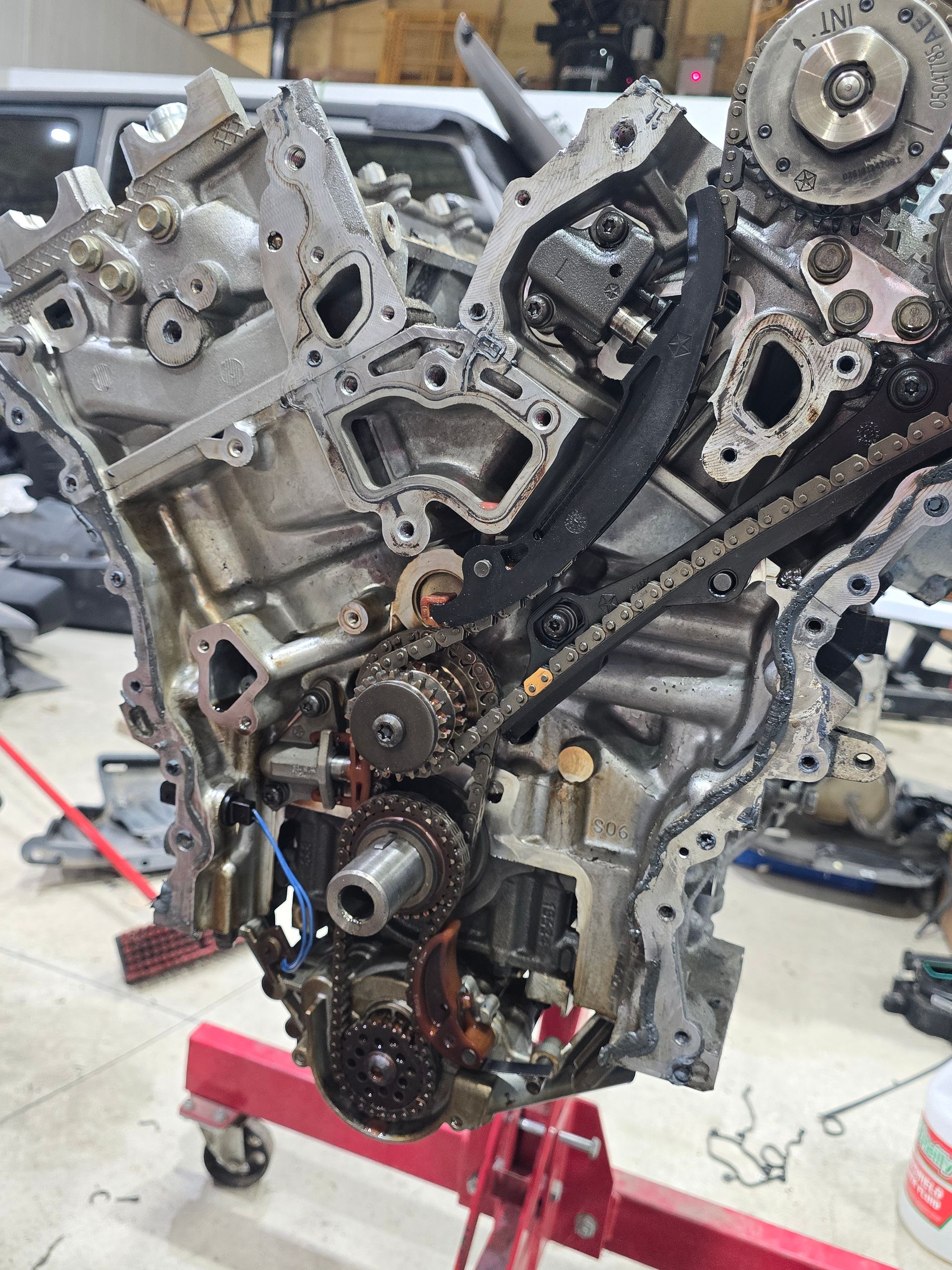 Exposed engine block on a red stand in a workshop, with chains and gears visible.