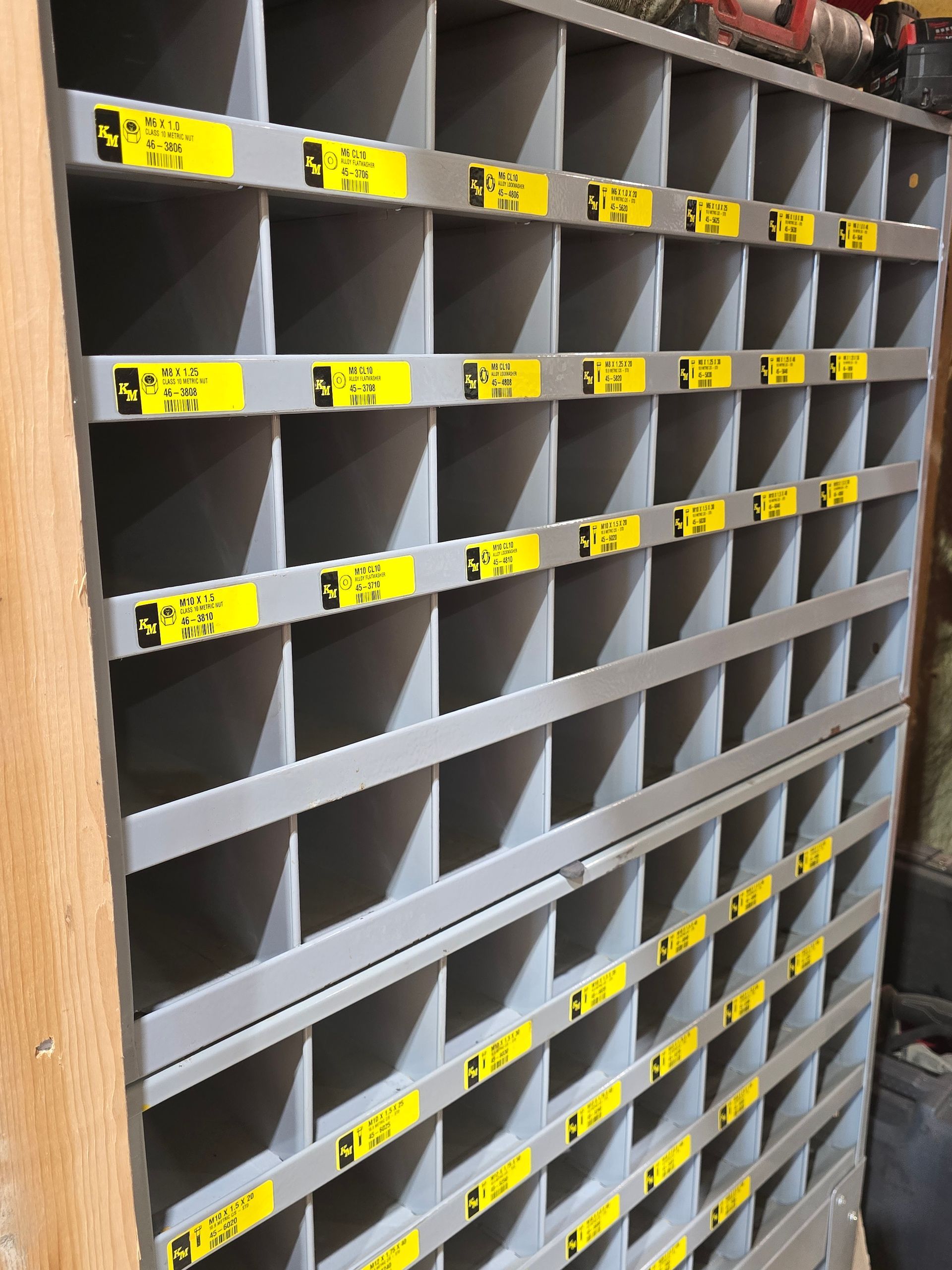 Grey cubby storage shelf with many labeled compartments in a workshop or mailroom