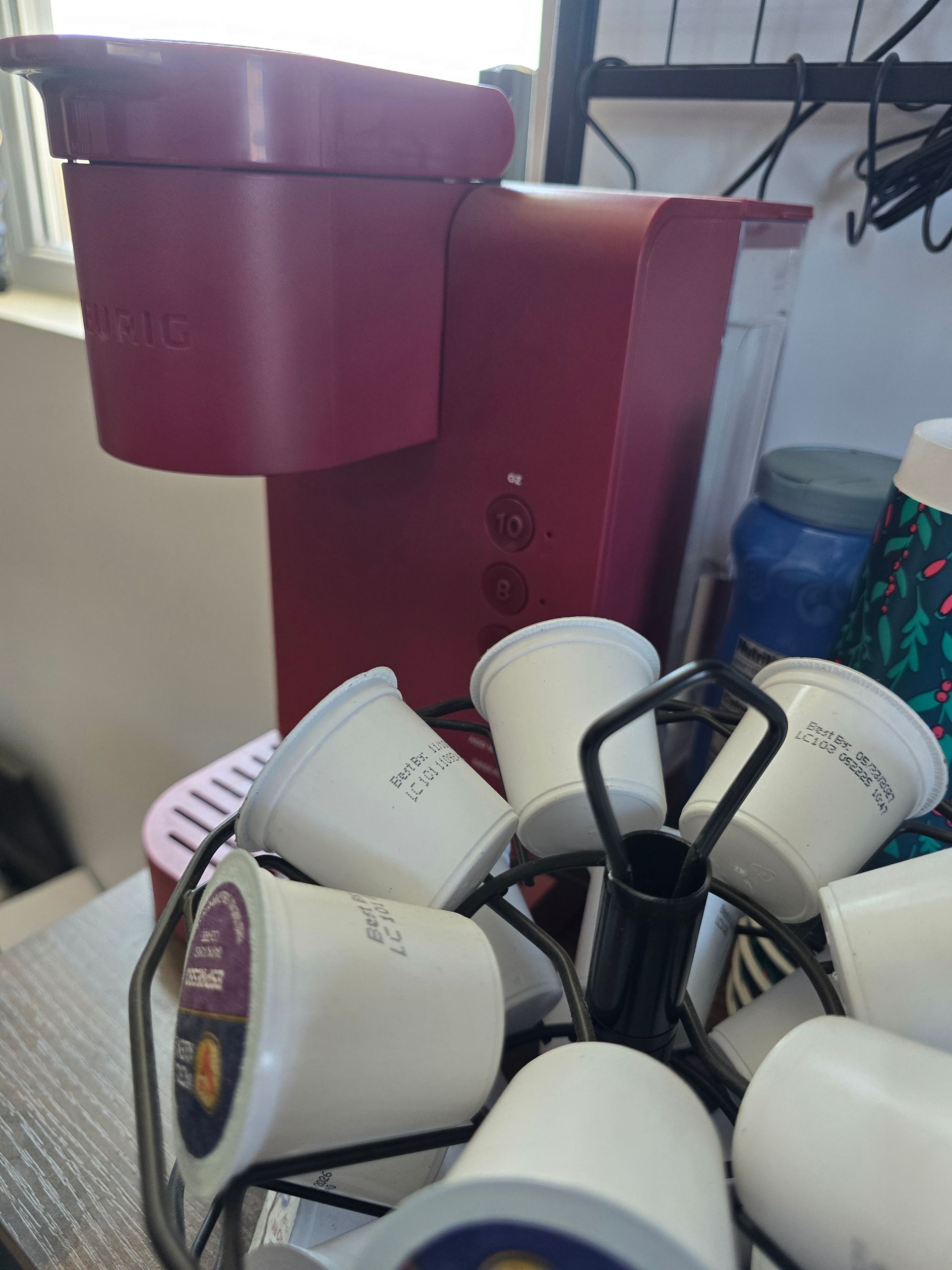 Coffee maker with multiple white cups arranged around a black holder and a red container in the background
