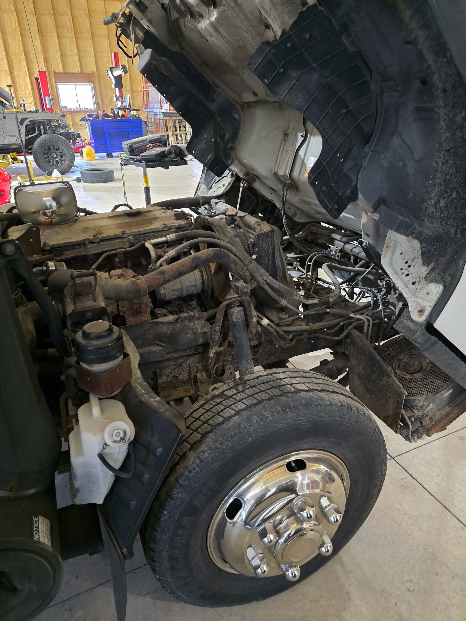 Mechanic lifting the hood of a blue truck in a garage; wearing a blue cap and orange gloves.