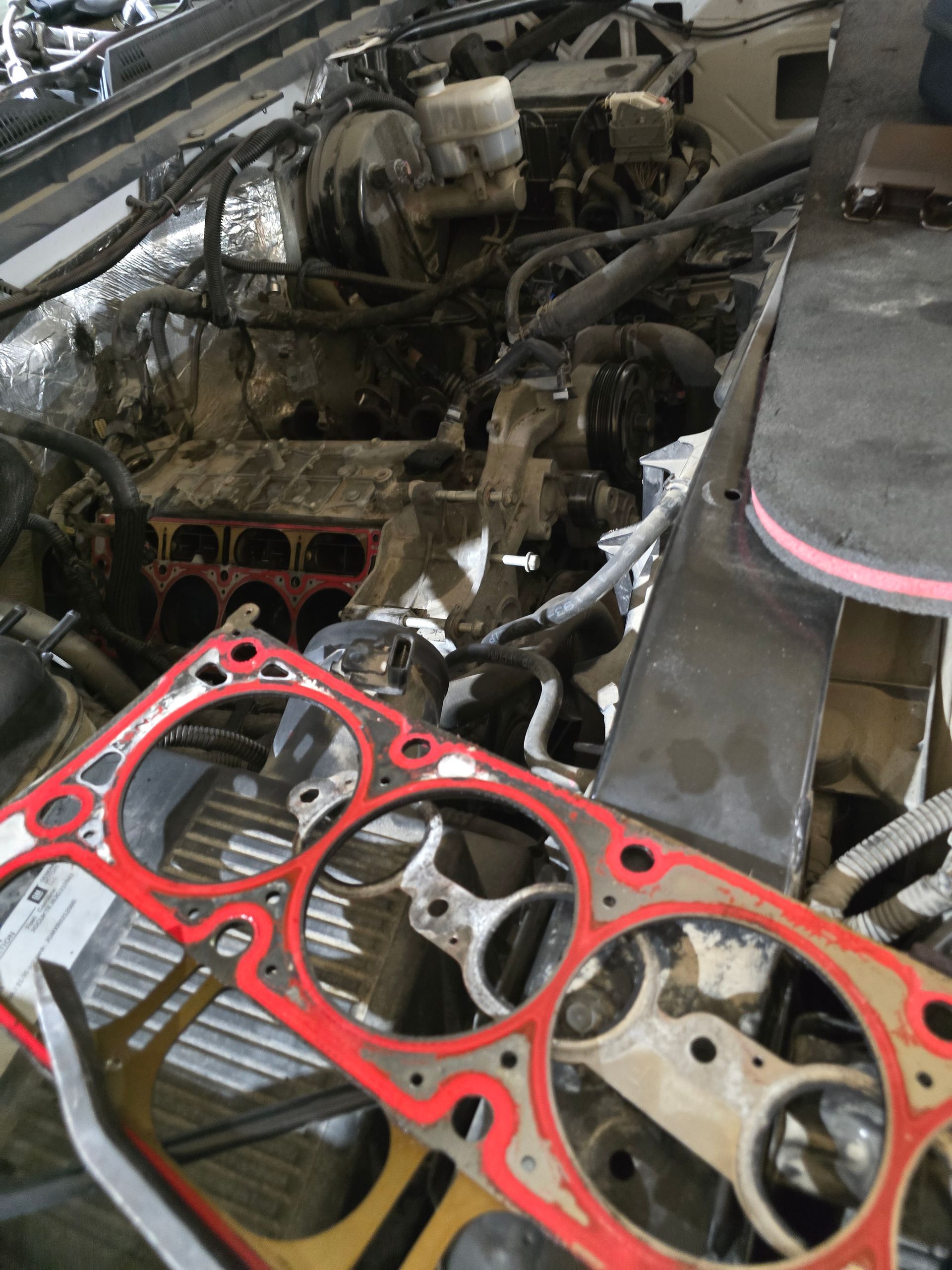Mechanic using a wrench on a car engine, another person taking notes nearby.
